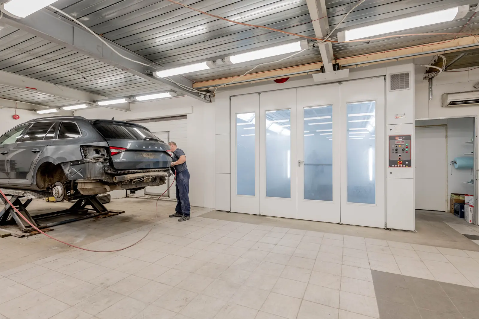 Damaged wagon on a lift beside a spray booth during a major collision repair