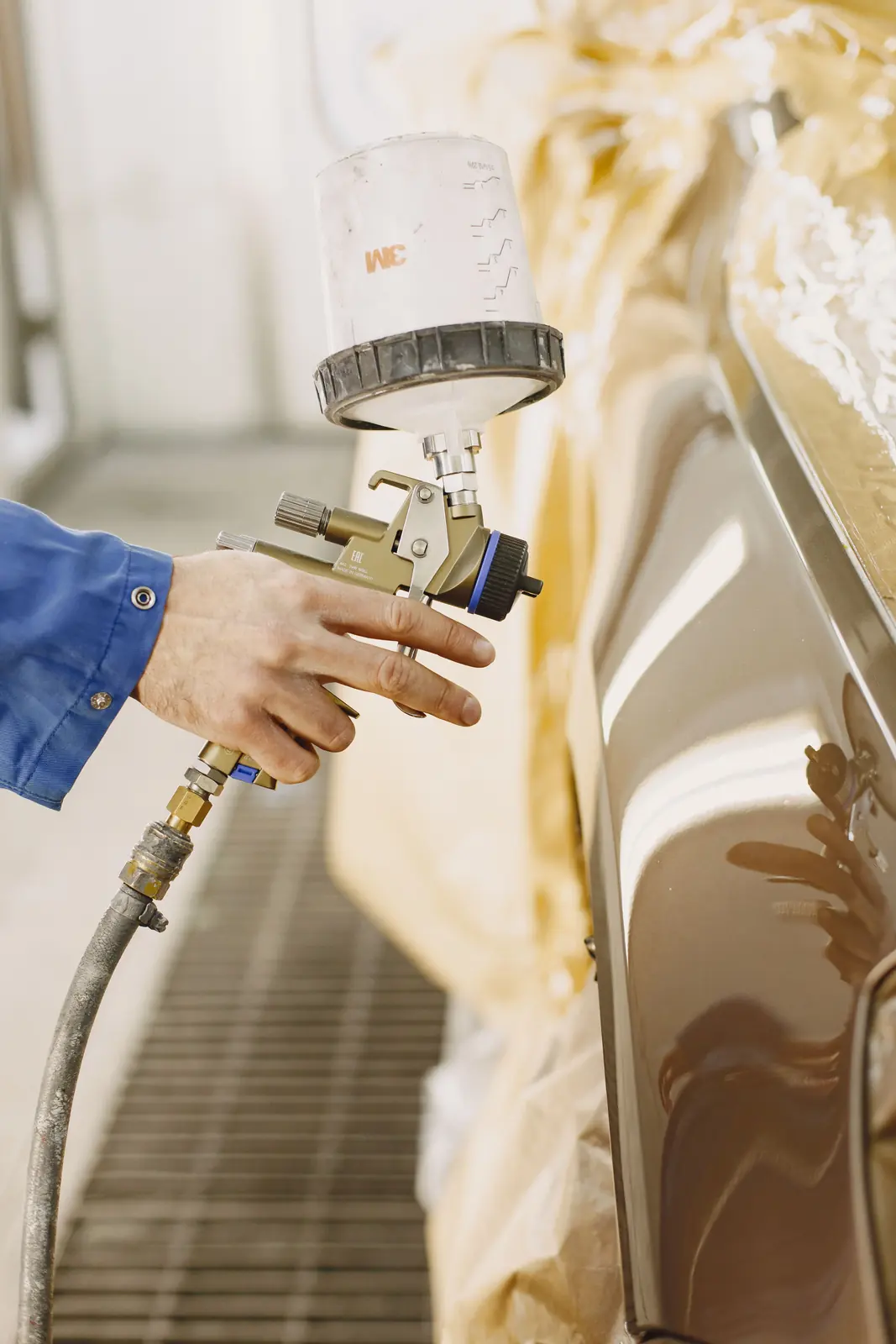 Spray gun applying paint to a masked car panel